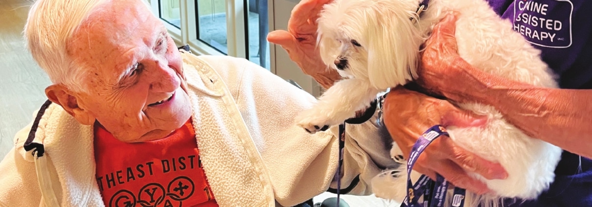 senior man petting a maltese dog as part of canine assisted therapy